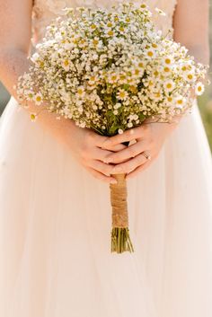 a woman in a wedding dress holding a bouquet of daisies and baby's breath