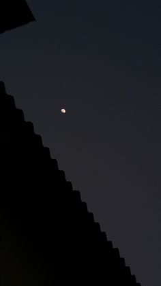 the moon is visible in the dark sky above a building's roof top, as seen from below