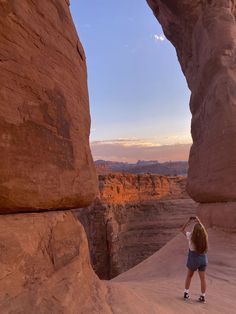 a woman standing in the middle of a desert area with rocks and cliffs behind her