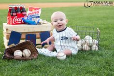 a baby sitting in the grass with baseballs and soda