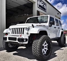 a white jeep is parked in front of a building with large tires and rims