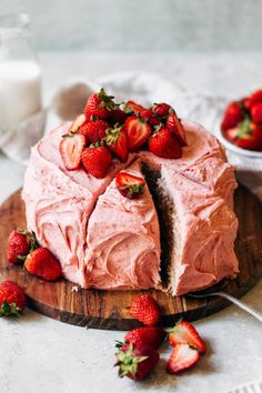 a cake with pink frosting and sliced strawberries on the plate next to it