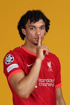 a young man in a red soccer jersey is posing for the camera with his finger to his mouth