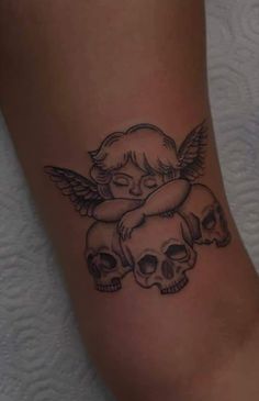 a tattoo with two skulls and an angel on the back of its leg, one is holding a baby