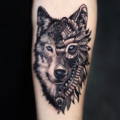 a black and white tattoo with a wolf's head on the left arm, surrounded by feathers