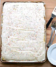 a sheet cake with white frosting and sprinkles on it next to two forks