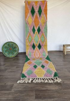 a multicolored rug with tassels and fringe on the floor in front of a white wall