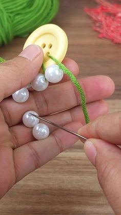 two hands are holding buttons and needles on a wooden surface with yarn in the background