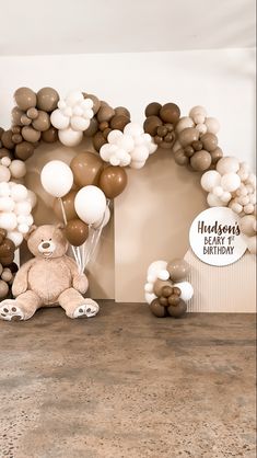 a teddy bear sitting in front of a bunch of balloons and a birthday sign on the wall