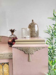 a pink table topped with a vase next to a green plant and potted plants