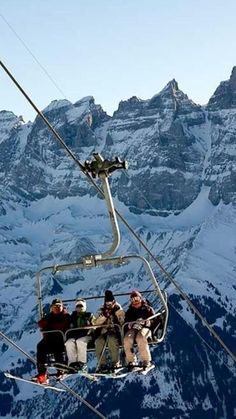 four people on a ski lift in front of snow covered mountain tops, with mountains in the background