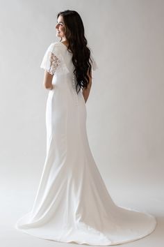 a woman in a white wedding dress standing with her back to the camera and looking off into the distance