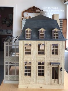 a doll house with windows and doors on top of a wooden table in front of a window