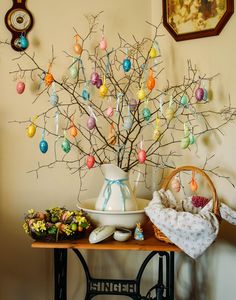 a table topped with a vase filled with colorful eggs next to a wall hanging on the wall