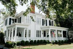 a large white house with black shutters and an american flag on the front porch