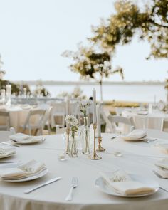 the table is set with white plates and silverware for an elegant wedding reception by the water