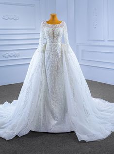 a white wedding dress with long sleeves and beading on the skirt, is displayed in front of a mannequin