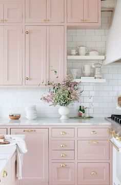 a kitchen with pink cabinets and white counter tops, gold pulls on the handles to match the cabinetry