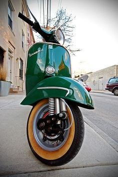 a green scooter parked on the side of a street next to a building