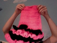 a woman holding up a pink crocheted hat with black ruffles on it