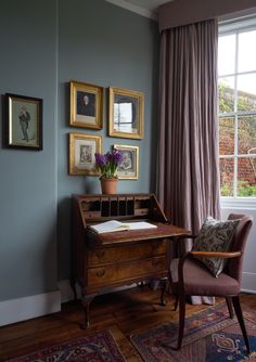 a room with a desk, chair and pictures on the wall above it in front of a window