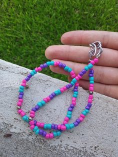 a person is holding two bracelets made out of beads and silver metal findings on a rock