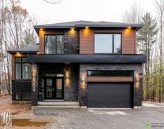 a two story house in the woods with lights on it's windows and doors