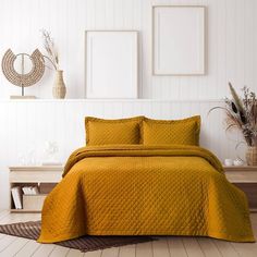 a bed with yellow bedspread and two pictures on the wall in a white room