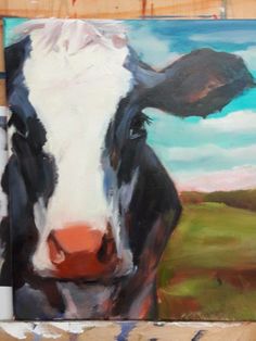 a painting of a black and white cow is on the easel next to some paintbrushes