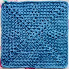 a blue crocheted square sitting on top of a flowered tablecloth with pink and white flowers