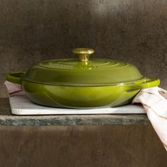 a green casserole dish sitting on top of a white towel next to a brown wall