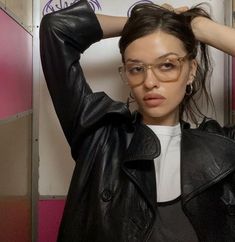 a woman wearing glasses and a leather jacket is posing for the camera with her hands on her head