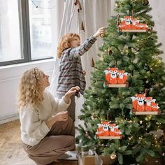 a woman and child decorating a christmas tree with red panda decorations on it's sides