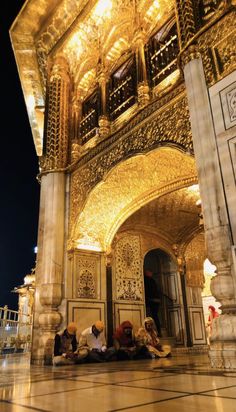 people sitting on the ground in front of an ornate building at night with bright lights