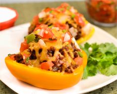 two stuffed peppers on a white plate with cilantro and tomatoes in the background