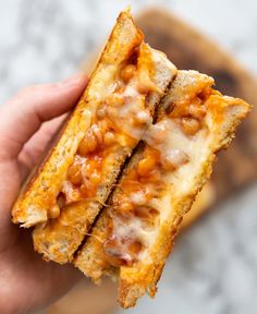 a person holding up a sandwich with cheese and meat on it in front of a piece of bread