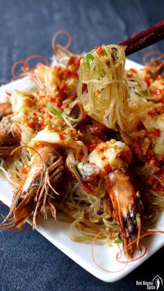 a plate full of noodles and shrimp with chopsticks