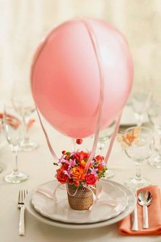 a pink balloon sitting on top of a white plate next to a vase filled with flowers