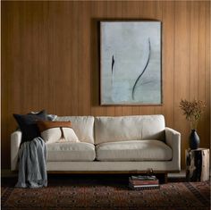 a living room with wood paneling and a white couch in front of a painting on the wall