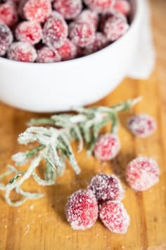 some sugared cranberries are sitting on a cutting board next to a bowl