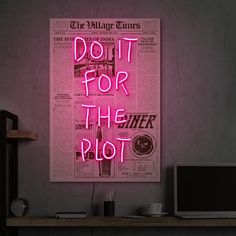 a pink neon sign that says do it for the plot on a wall next to a computer