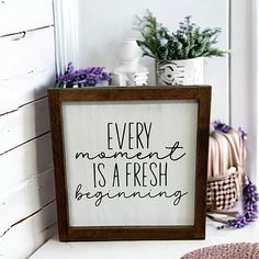 a sign that says every moment is a fresh beginning on the shelf next to a potted plant