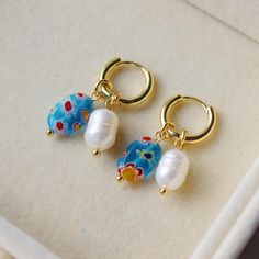 Millefiori Earrings - Blue Oval Beads and Fresh Water Pearls Bead dimensions: 12x8X3.5mm Made with 18K Gold hoops / hardware Detachable charms! Packaging: All products come with freebies and are packed by hand, so they make a great gifting experience! Postage: All orders are dispatched in 1-2 working days. Materials and Care: This item is 18K gold plated. Regularly polish and buff the metal using a soft (lint-free) cloth. Avoid contact with water / liquids. -------------------------------------- Handmade Dangle Huggie Earrings For Gifts, Blue Pearl Charm Earrings As Gift, Handmade Blue Huggie Earrings, Handmade Blue Huggie Hoop Earrings, Blue Huggie Earrings As Gift, Blue Dangle Huggie Earrings As Gift, Handmade Blue Huggie Jewelry, Blue Flower Earrings, Earrings Pearl