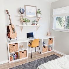 a bedroom with a desk, bookshelf and guitar on the wall above it