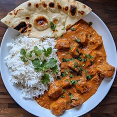 a white plate topped with rice and meat next to naan bread on top of a wooden table