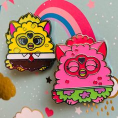 two pin badges sitting next to each other on top of a rainbow colored tablecloth