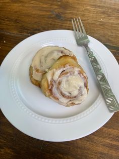 a white plate topped with two cinnamon rolls next to a fork and knife on top of a wooden table