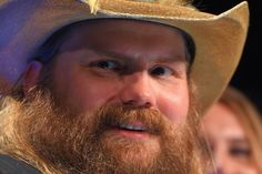 a bearded man wearing a cowboy hat and looking off to the side with two other people behind him