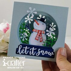 someone is holding up a card with a snowman in the center and flowers behind it