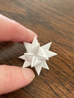 a hand holding an origami star on top of a wooden table next to a person's finger